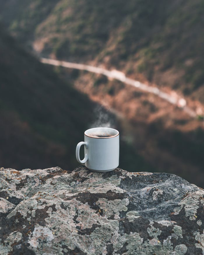 Steaming coffee mug on a rocky surface with a blurred scenic background in Athens, Greece.